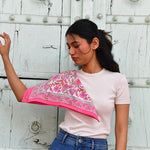 Petit foulard Andromaque Rose porté sur l'épaule, devant une porte blanche