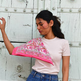 Petit foulard Andromaque Rose porté sur l'épaule, devant une porte blanche