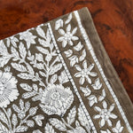 Gros plan sur le motif fleuri du petit foulard Antioche Kaki, posé sur du bois