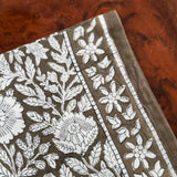 Gros plan sur le motif fleuri du petit foulard Antioche Kaki, posé sur du bois