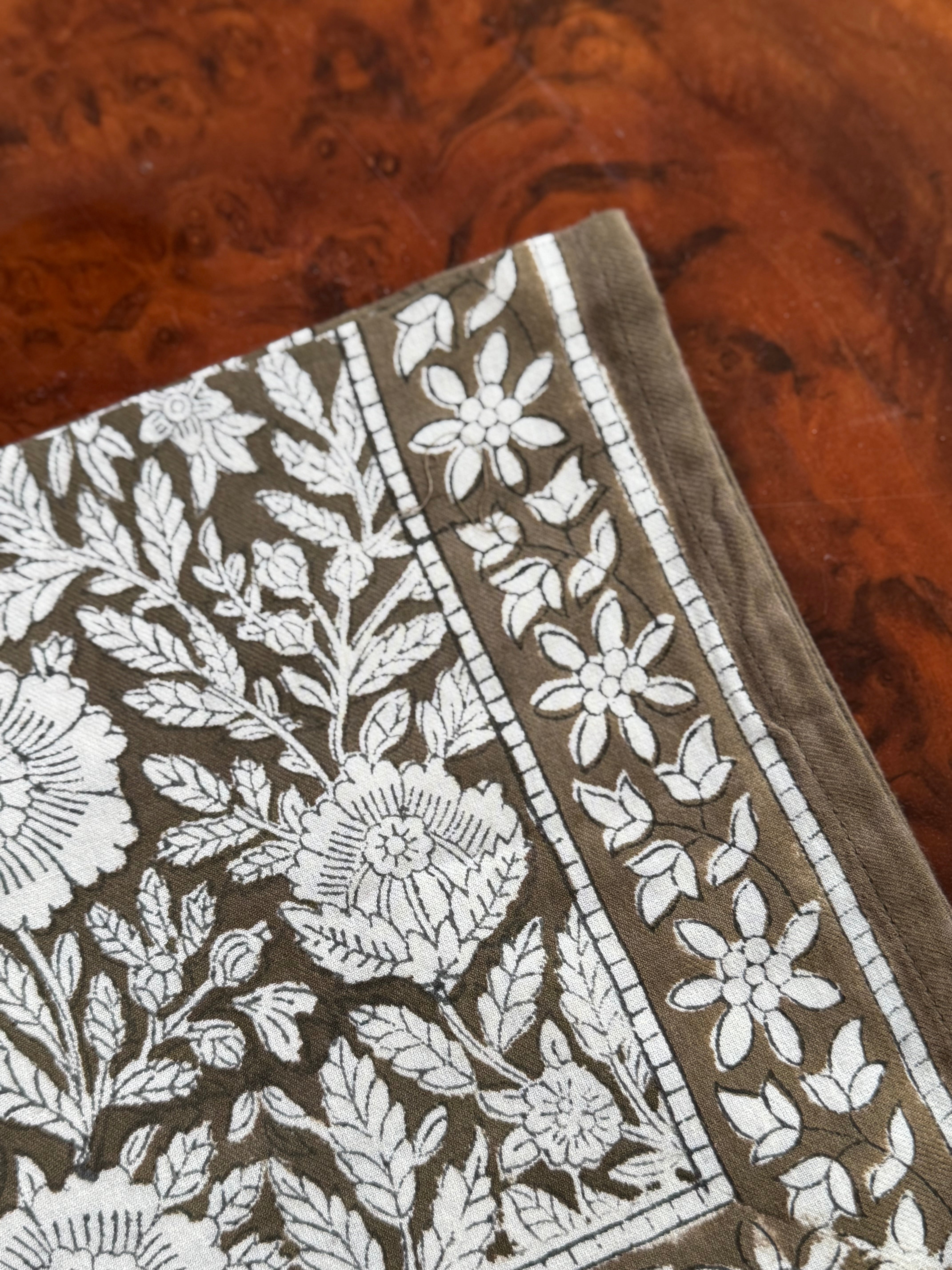 Gros plan sur le motif fleuri du petit foulard Antioche Kaki, posé sur du bois