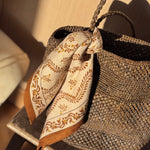 Petit foulard Antoinette Beige à bordure caramel noué à l'anse d'un panier