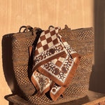 Petit foulard Checks Bistre noué sur un panier tressé posé sur un tabouret