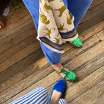 Petit foulard Fauve Tabac tenu à la main, au-dessus d'un parquet en bois