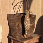 Petit foulard Mercure Bistre de byzantine noué à un panier en osier sur un tabouret