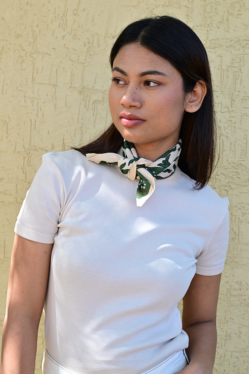 Petit foulard écru et vert roulé et noué autour du cou d’une jeune femme