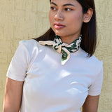 Petit foulard écru et vert roulé et noué autour du cou d’une jeune femme