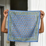 Petit foulard Séléné Bleu horizon déplié, tenu devant une porte