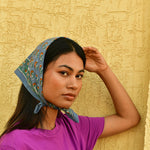 Petit foulard Séléné Bleu horizon porté en fichu, main posée sur la tête