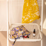 Petite trousse beauté N°113 Bleu couchée sur une chaise blanche, avec un sérum