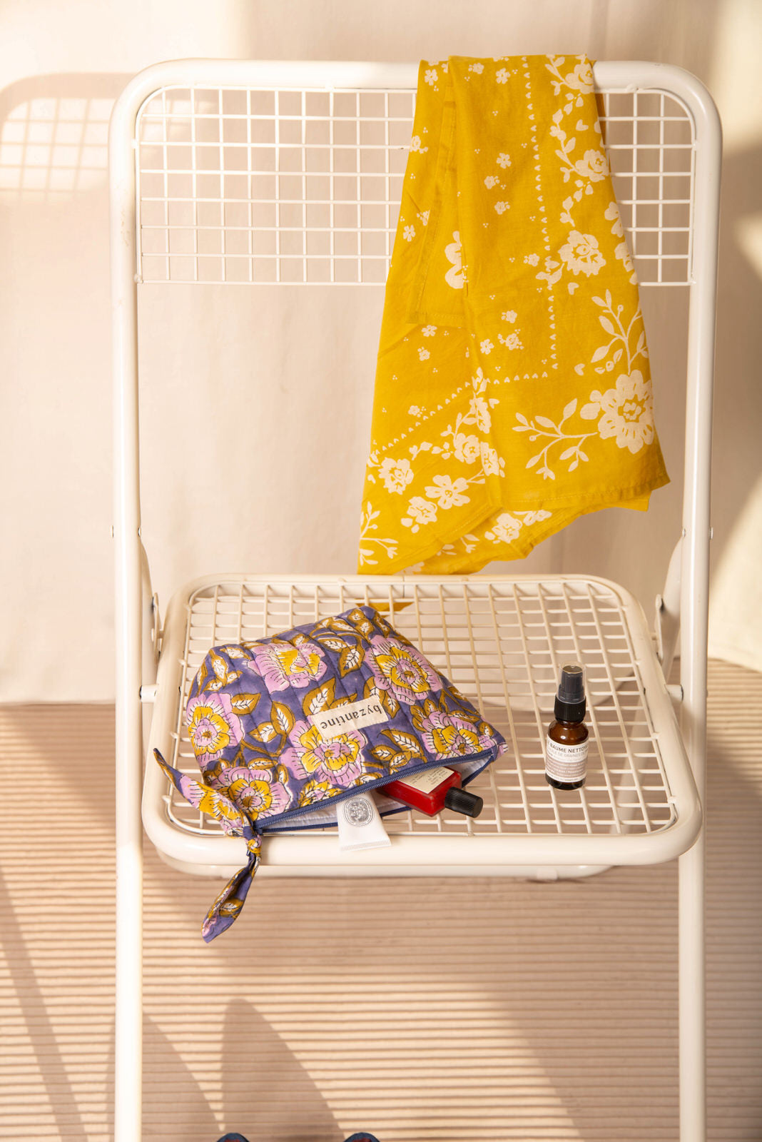 Petite trousse beauté N°113 Bleu couchée sur une chaise blanche, avec un sérum