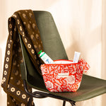 Petite trousse beauté Antioche Tomato sur une chaise verte, foulard marron sur le dossier