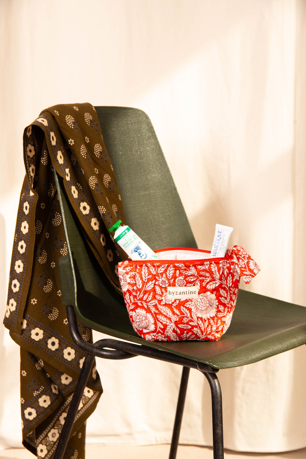 Petite trousse beauté Antioche Tomato sur une chaise verte, foulard marron sur le dossier