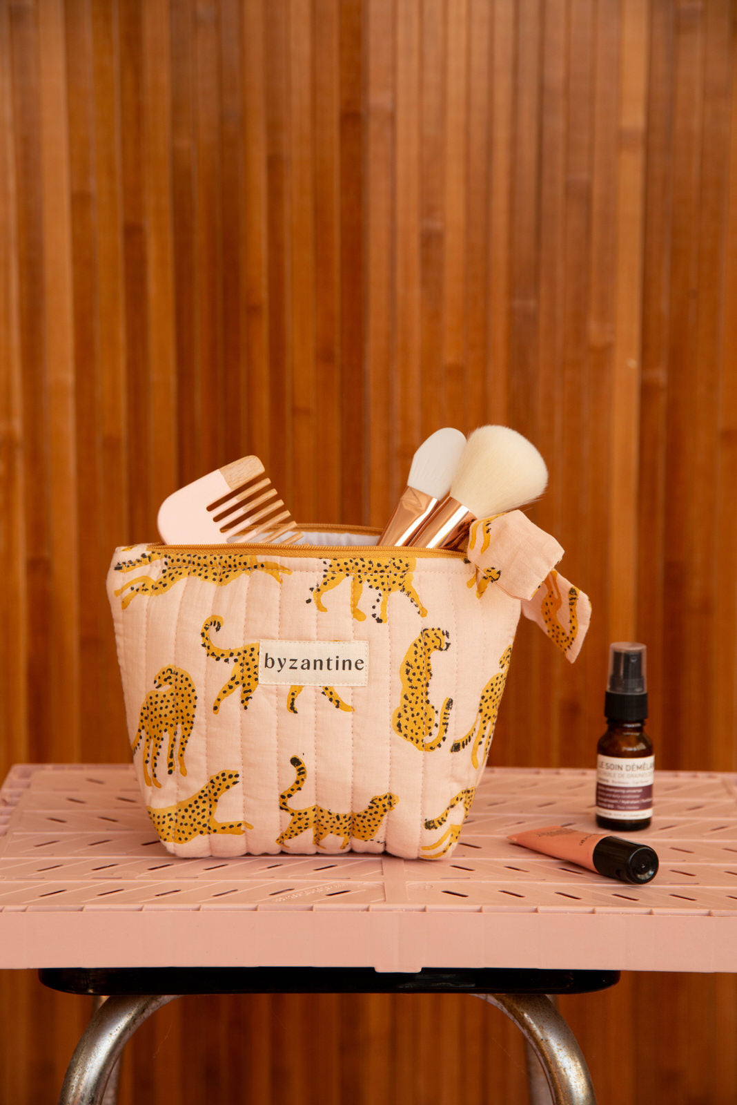 Petite trousse beauté Fauve Rose remplie de pinceaux, posée sur une caisse rose