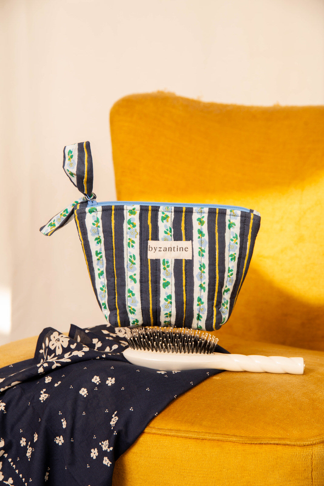 Petite trousse beauté Flora Bleu marine à nœud, avec une brosse, sur un fauteuil