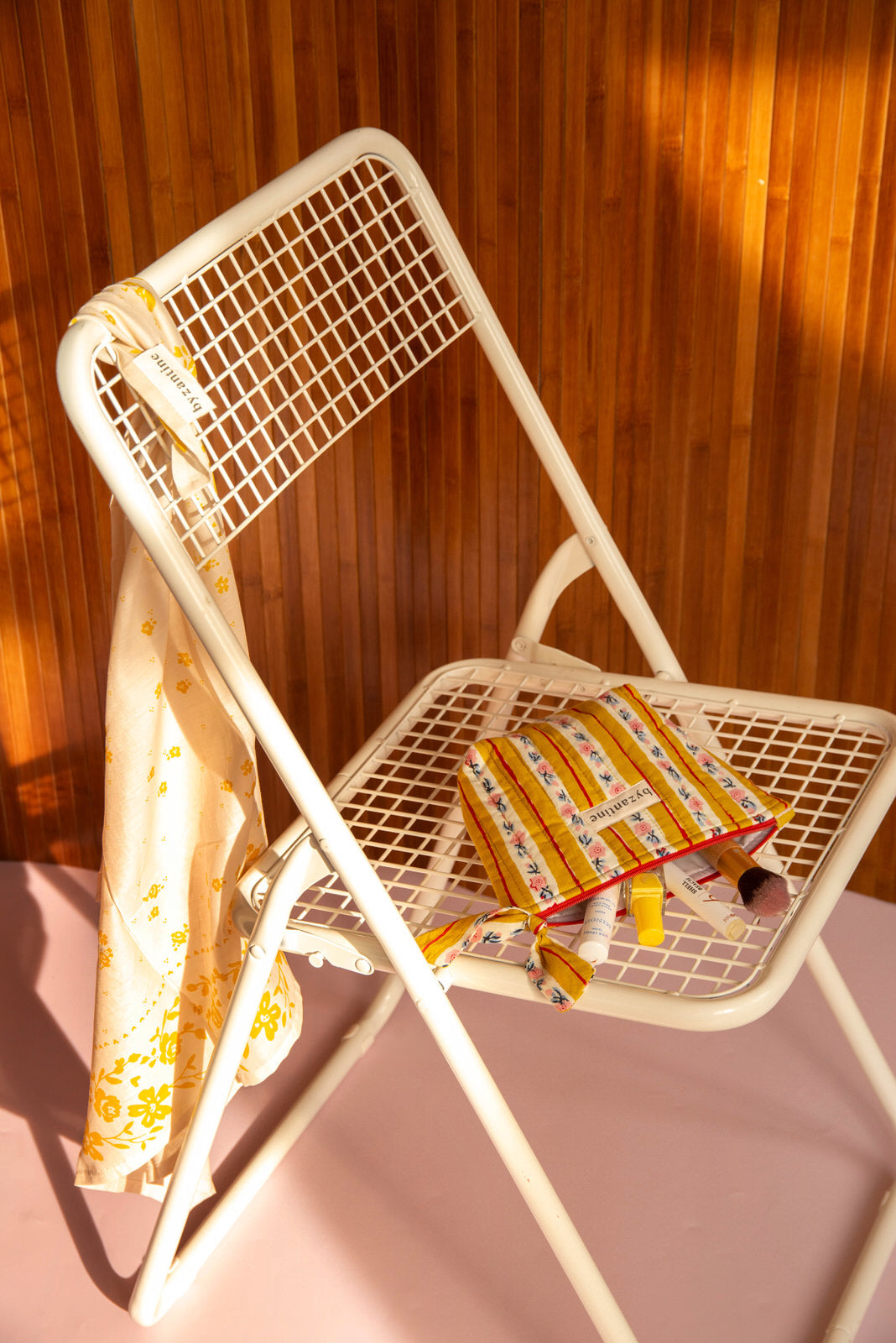 Petite trousse beauté Flora Passion sur une chaise blanche, foulard fleuri sur le dossier