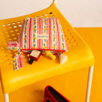 Petite trousse beauté Flora Rose à nœud ouverte sur une chaise jaune, soins éparpillés et ballerines rouges