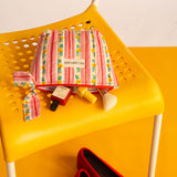 Petite trousse beauté Flora Rose à nœud ouverte sur une chaise jaune, soins éparpillés et ballerines rouges