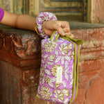 Petite trousse de toilette Carthage Lilas tenue à la main avec un chouchou assorti