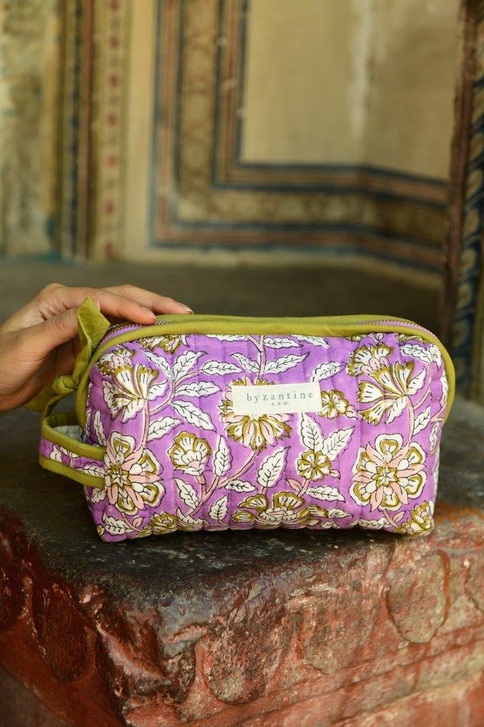 Petite trousse de toilette Carthage Lilas posée sur un muret, main sur la trousse