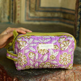 Petite trousse de toilette Carthage Lilas posée sur un muret, main sur la trousse