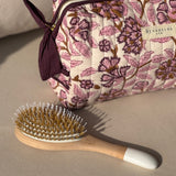 Trousse de toilette Carthage Prune posée à côté d'une brosse à cheveux