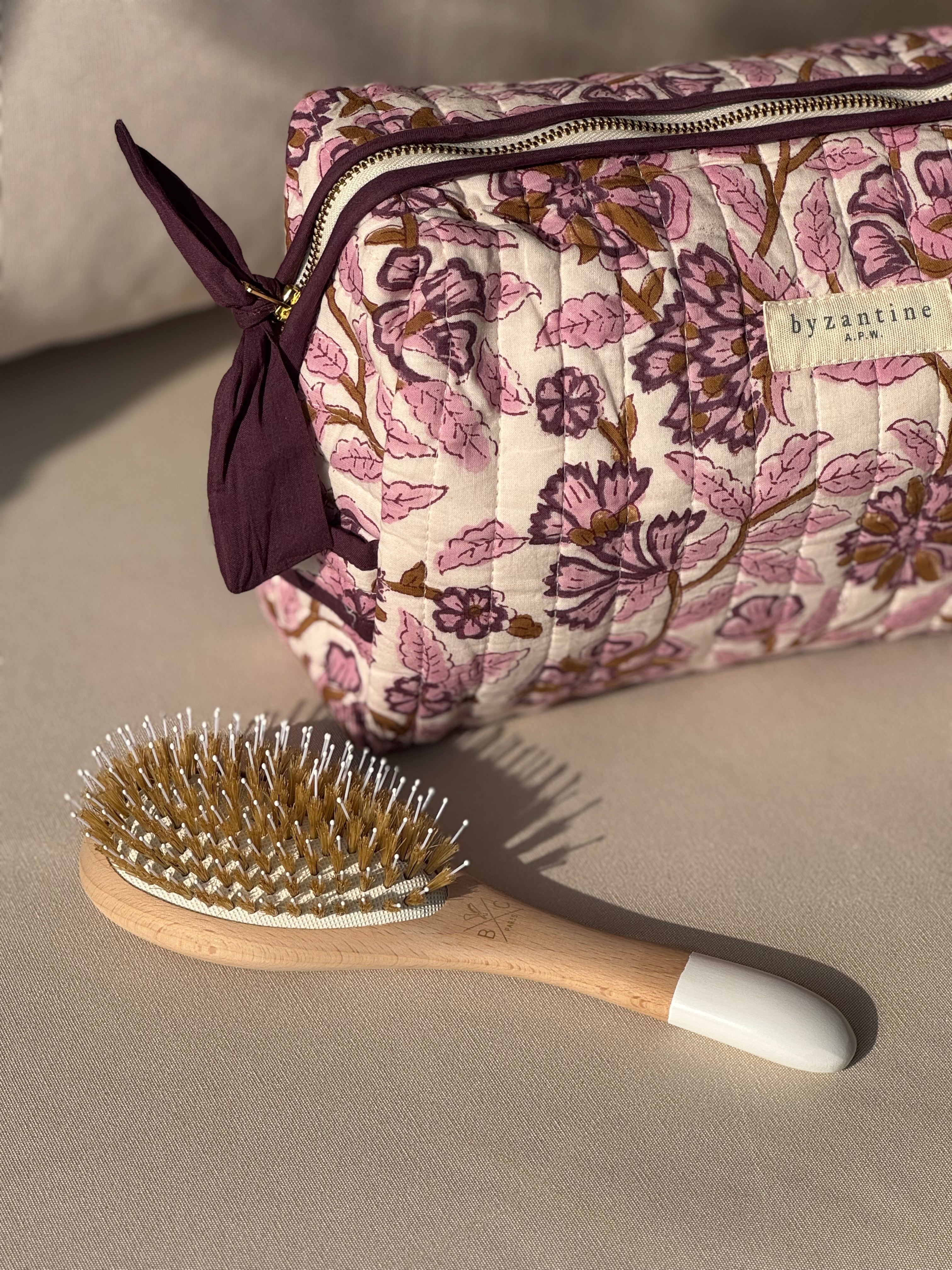 Trousse de toilette Carthage Prune posée à côté d'une brosse à cheveux