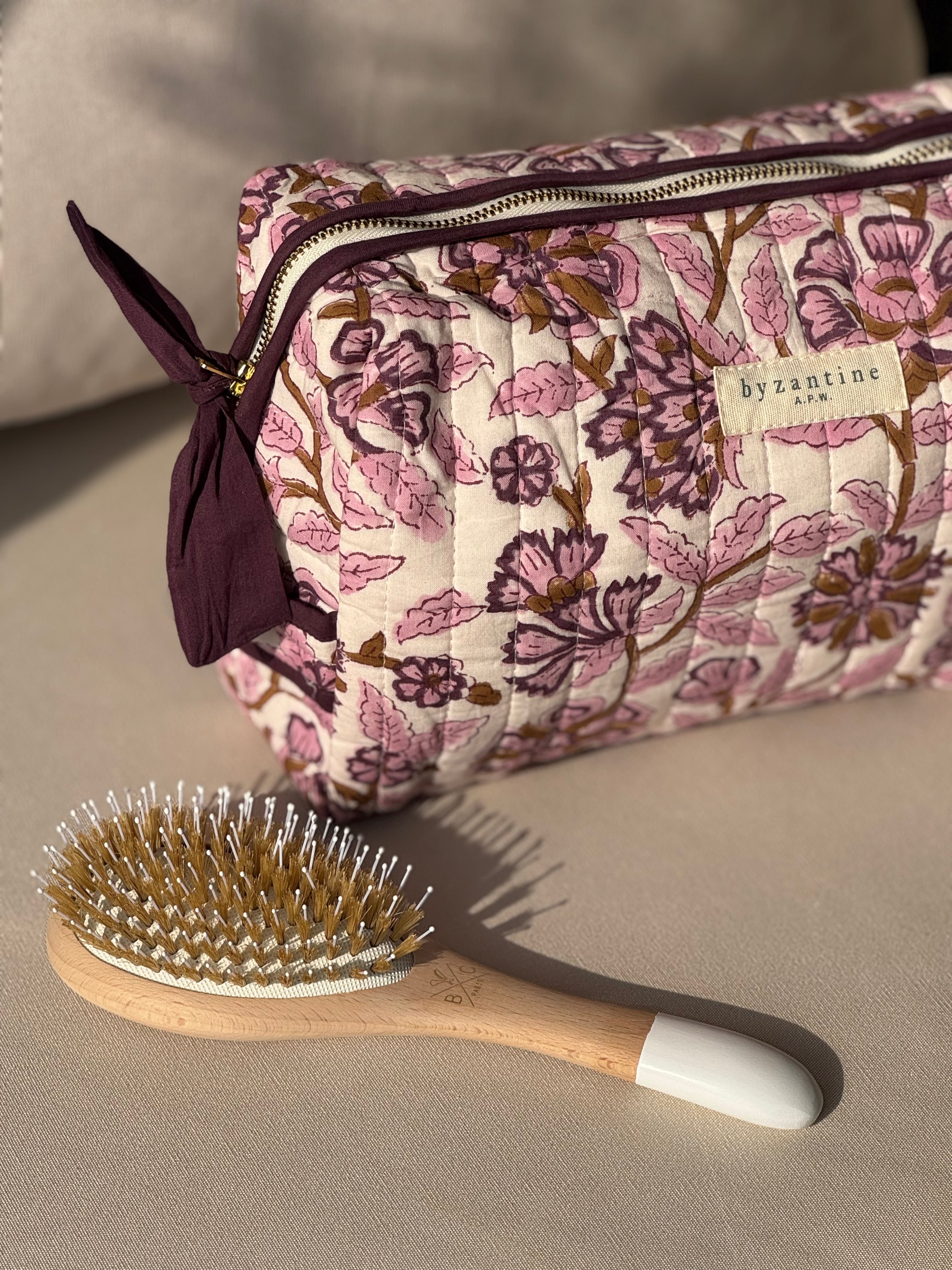 Trousse de toilette Carthage Prune posée sur un canapé, avec une brosse à cheveux