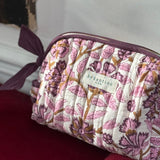 Trousse de toilette Carthage Prune posée sur un velours rouge