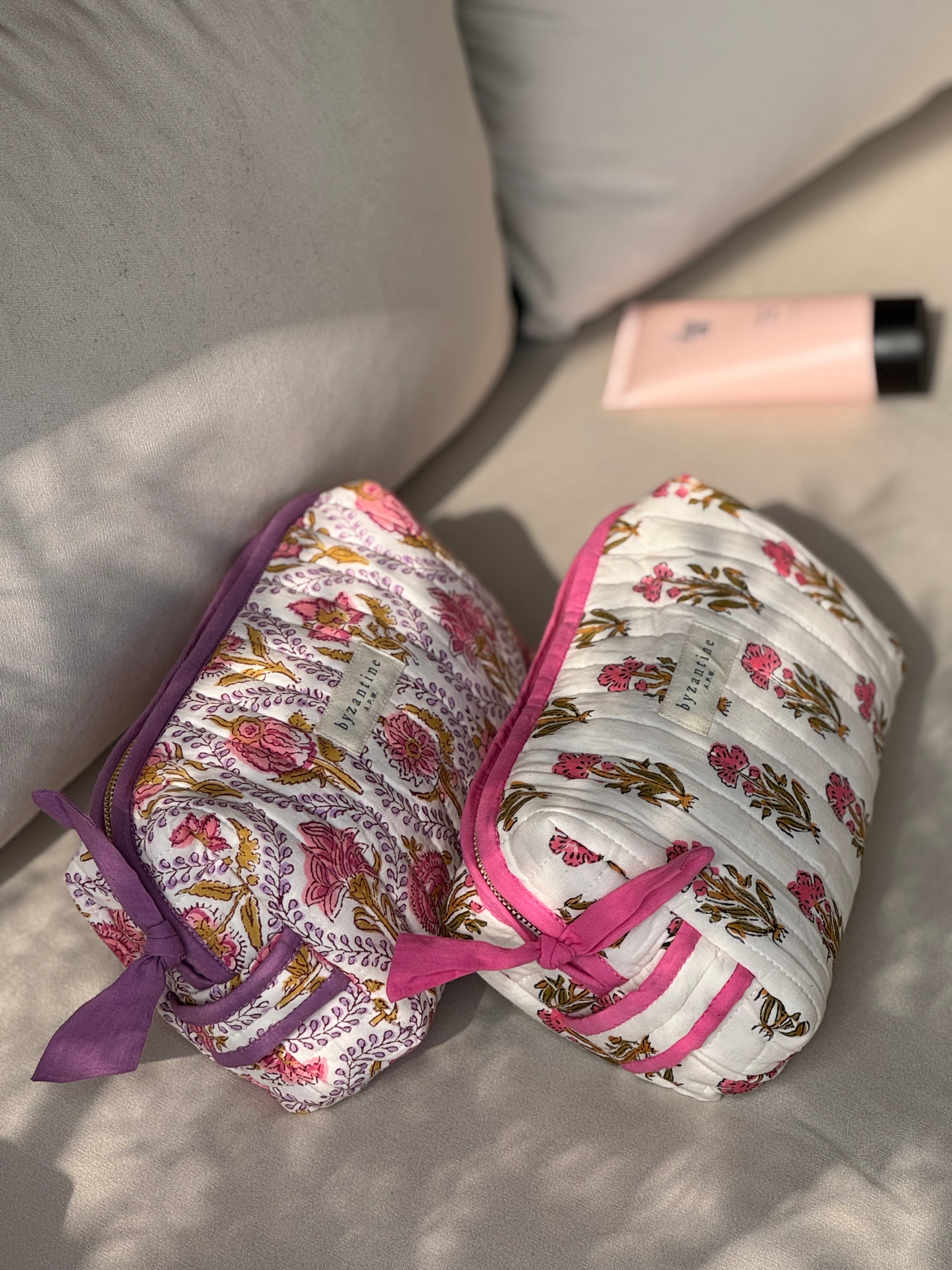 Duo de trousses de toilette Éphèse Rose couchées sur un canapé