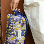 Petite trousse de toilette N°113 Bleu tenue à la main, pantalon blanc