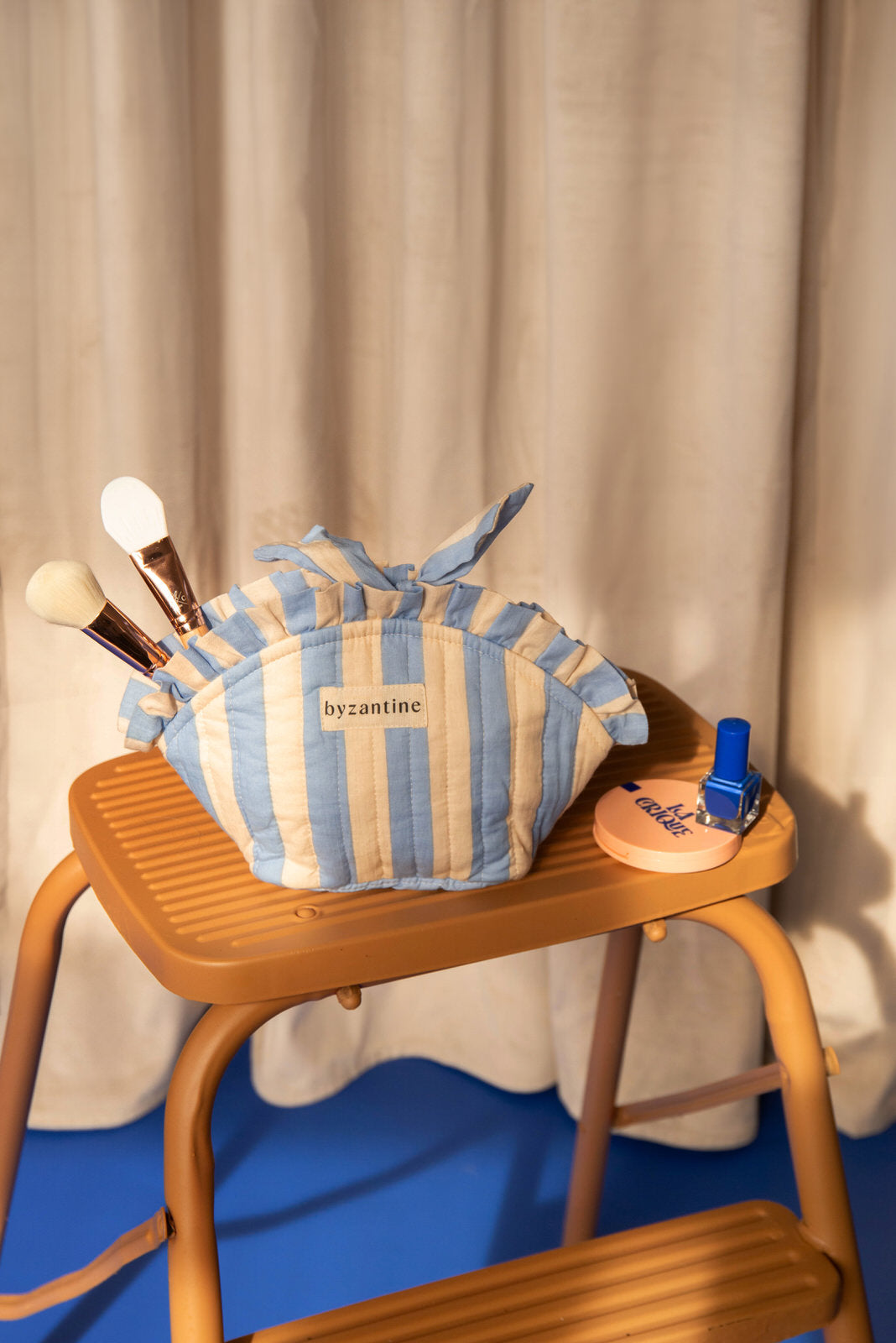 Petite trousse froufrou Pacha Bleu ciel nouée, avec pinceaux et vernis, sur un escabeau