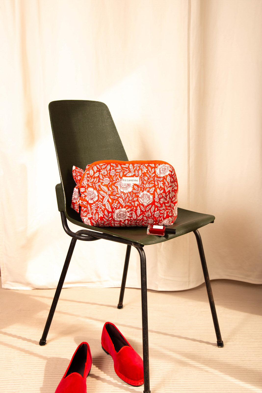 Petite trousse de toilette Antioche Tomato sur une chaise vert foncé, ballerines rouges