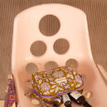 Petite trousse de toilette Carthage Kaki sur une chaise rose, flacons posés devant