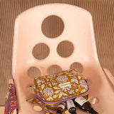 Petite trousse de toilette Carthage Kaki sur une chaise rose, flacons posés devant