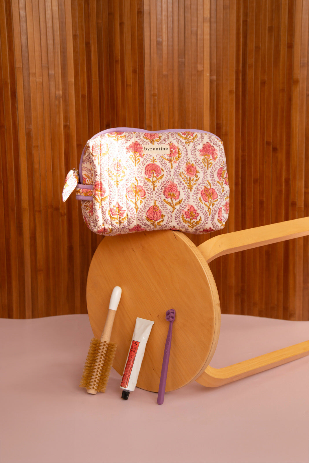 Petite trousse de toilette Éphèse Rose sur un tabouret renversé, mascaras au sol