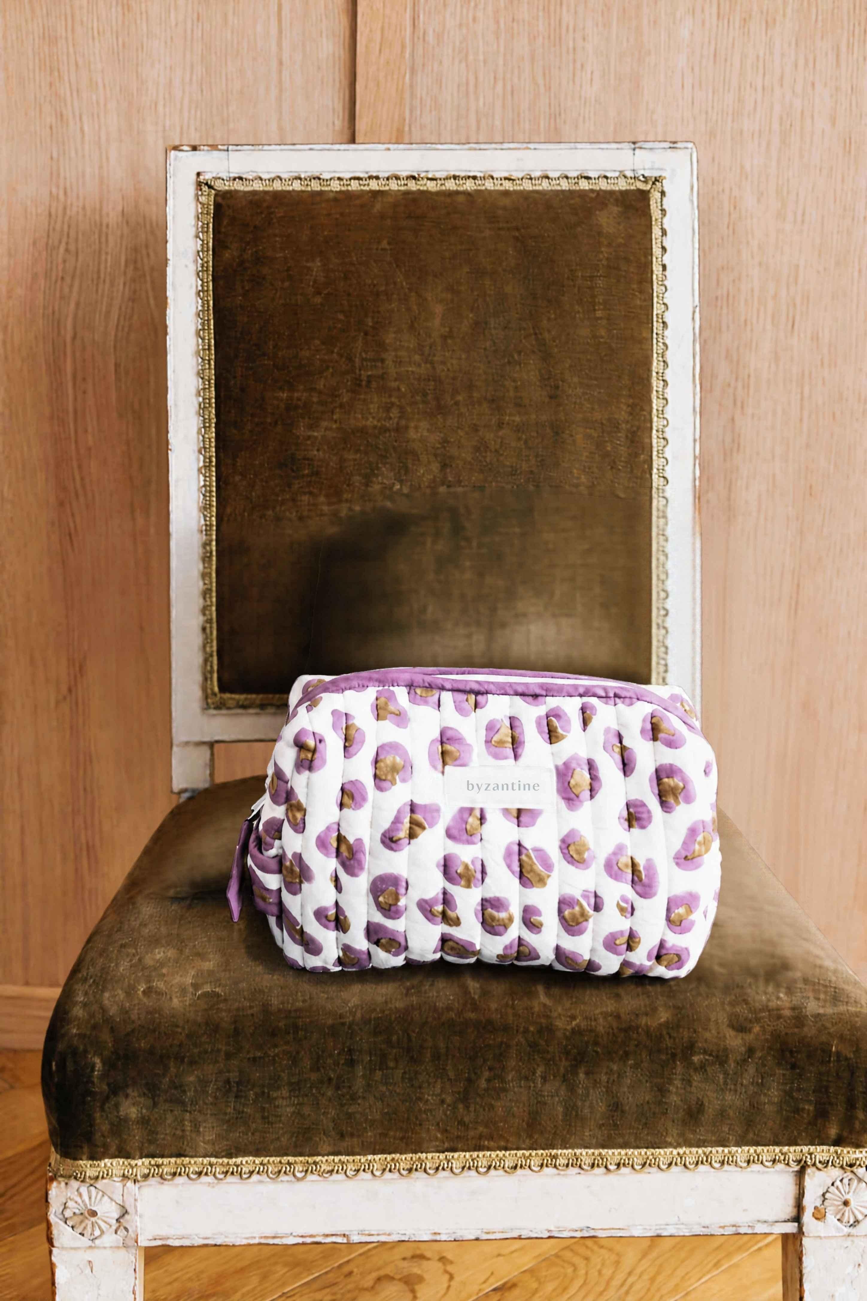 Petite trousse de toilette Léopard Écru et Violet de byzantine sur une chaise en velours