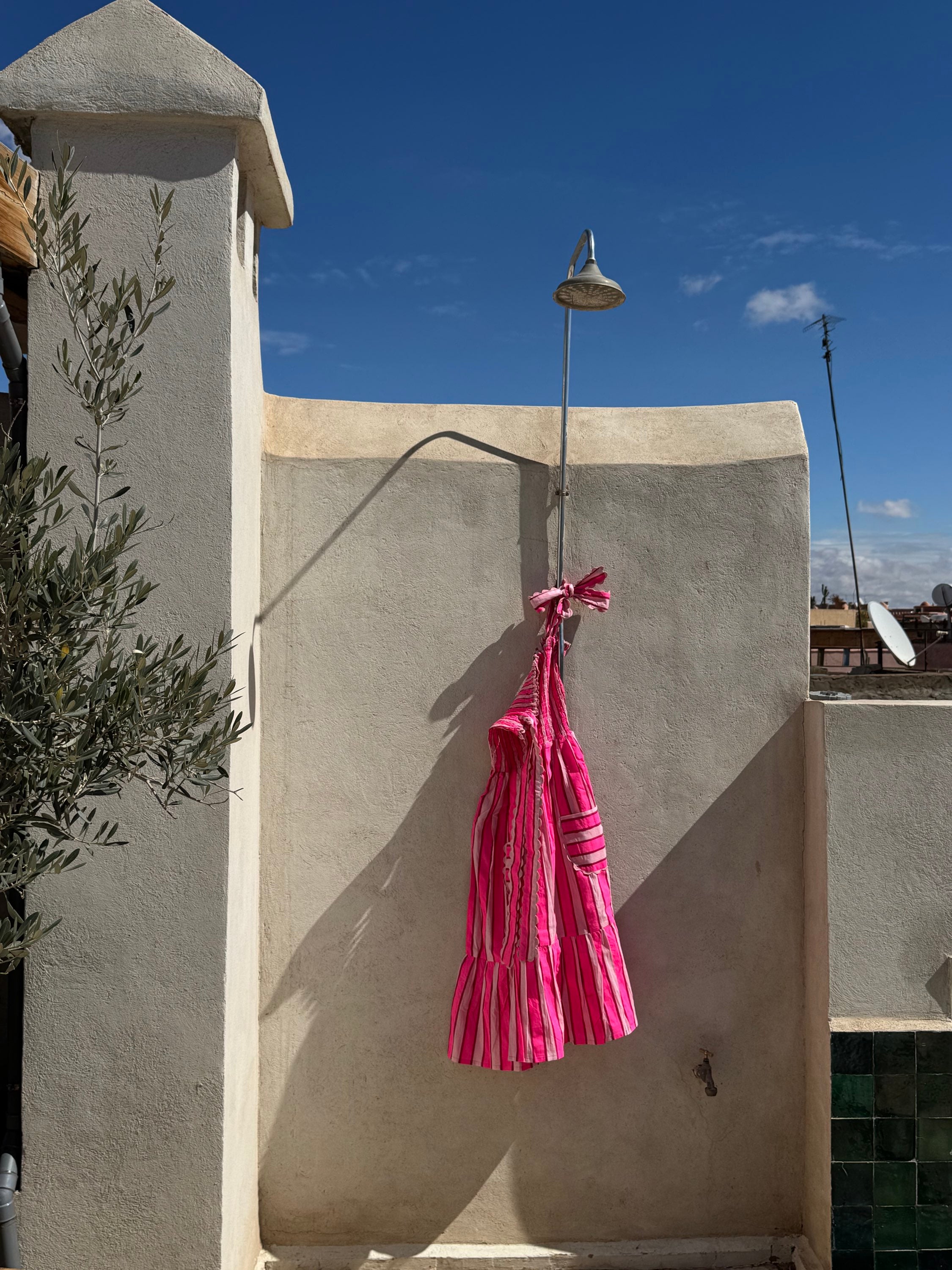 Robe Froufrou Fluo Pink suspendue à une douche extérieure sur un toit