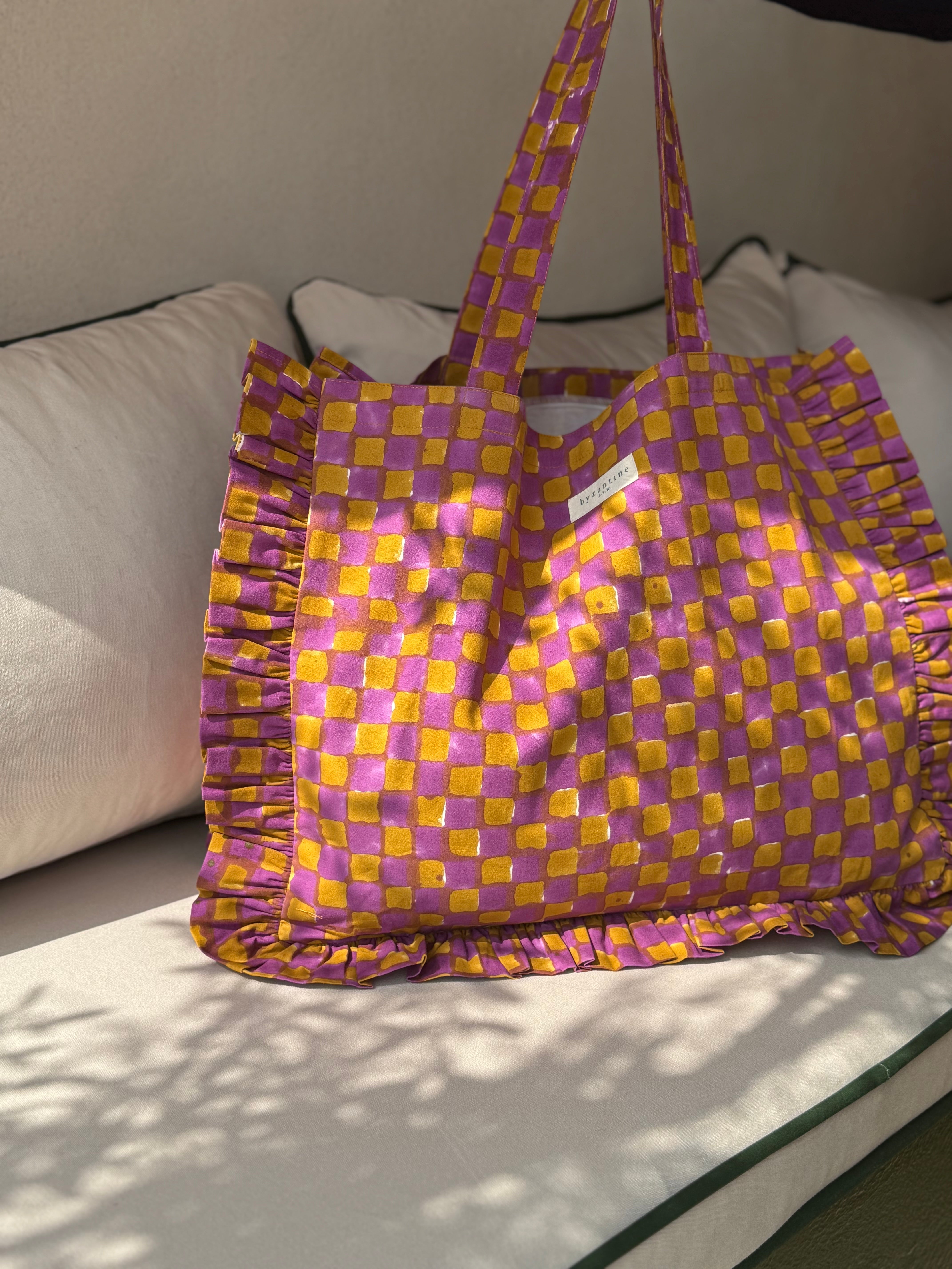 Sac froufrou Moutarde violet posé sur un canapé, damier violet et moutarde, volants sur les côtés