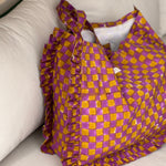 Sac froufrou Moutarde violet posé sur un canapé, damier imprimé et volants sur les côtés