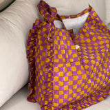 Sac froufrou Moutarde violet posé sur un canapé, damier imprimé et volants sur les côtés