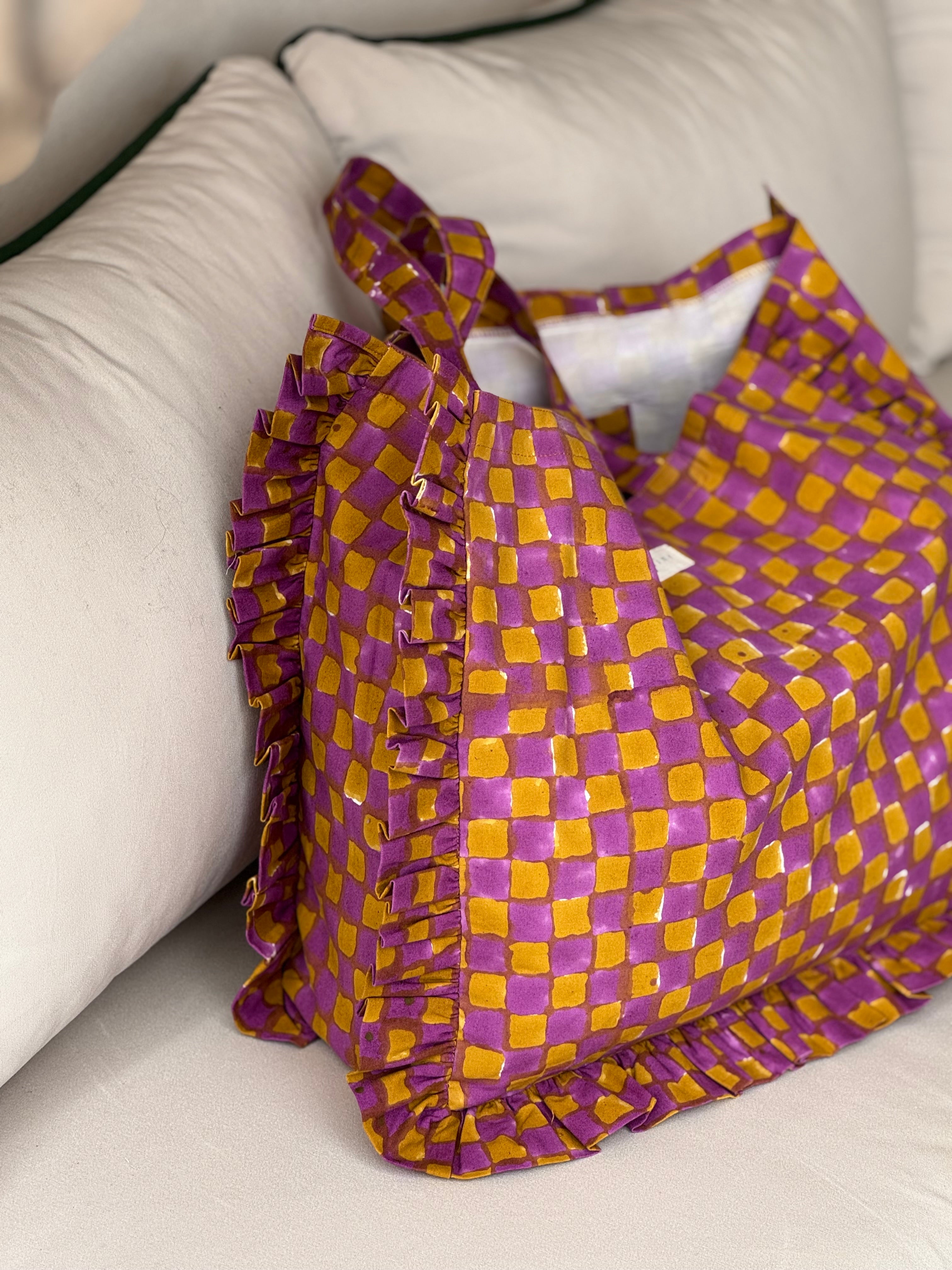 Sac froufrou Moutarde violet posé sur un canapé, damier imprimé et volants sur les côtés
