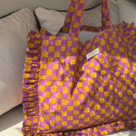 Sac froufrou Moutarde violet à damier, anses longues, étiquette Byzantine, posé au soleil sur un canapé