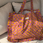 Sac froufrou à damier violet et moutarde de face, volants sur le pourtour, posé sur un canapé blanc