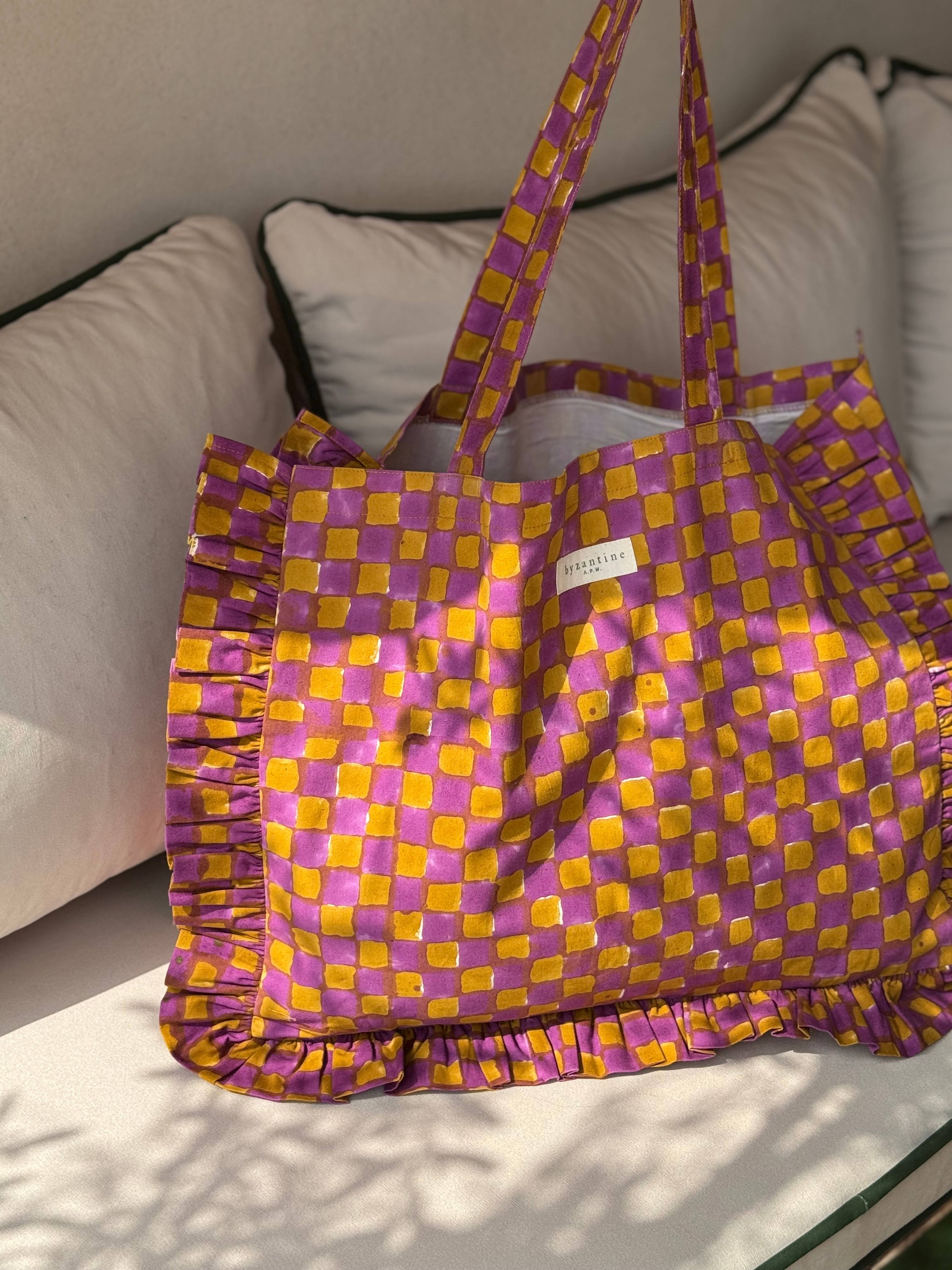 Sac froufrou à damier violet et moutarde de face, volants sur le pourtour, posé sur un canapé blanc