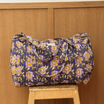 Sac weekend matelassé N°113 Bleu de Byzantine, fleurs jaunes et lilas sur fond bleu, posé sur un tabouret en bois