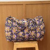 Sac weekend matelassé N°113 Bleu de Byzantine, fleurs jaunes et lilas sur fond bleu, posé sur un tabouret en bois