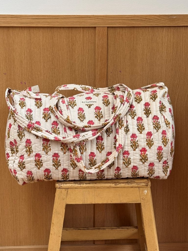 Sac weekend matelassé N°50 Rose de Byzantine, petites fleurs roses sur fond écru, posé sur un tabouret en bois
