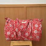Sac weekend matelassé Antioche Tomato de Byzantine, fleurs blanches sur fond rouge, posé sur un tabouret en bois