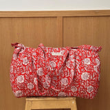 Sac weekend matelassé Antioche Tomato de Byzantine, fleurs blanches sur fond rouge, posé sur un tabouret en bois